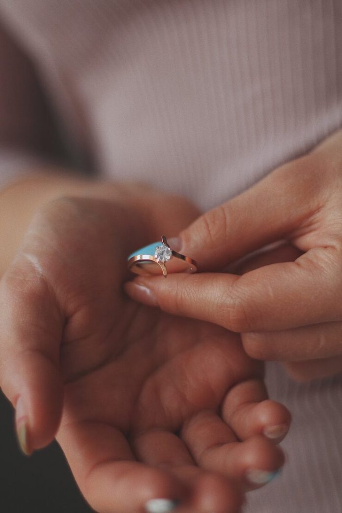 vertical-closeup-shot-female-holding-beautiful-gold-diamond-ring_181624-15326